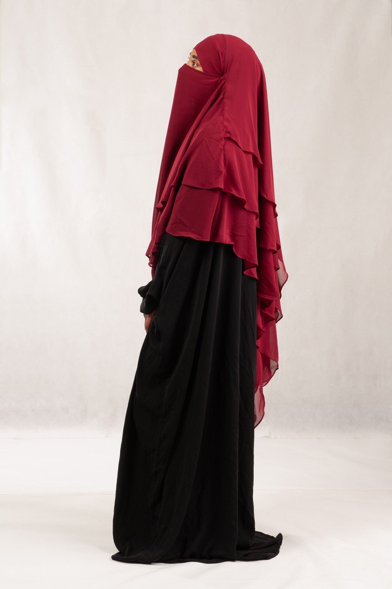 Person wearing a red hijab khimar and black dress on a white background