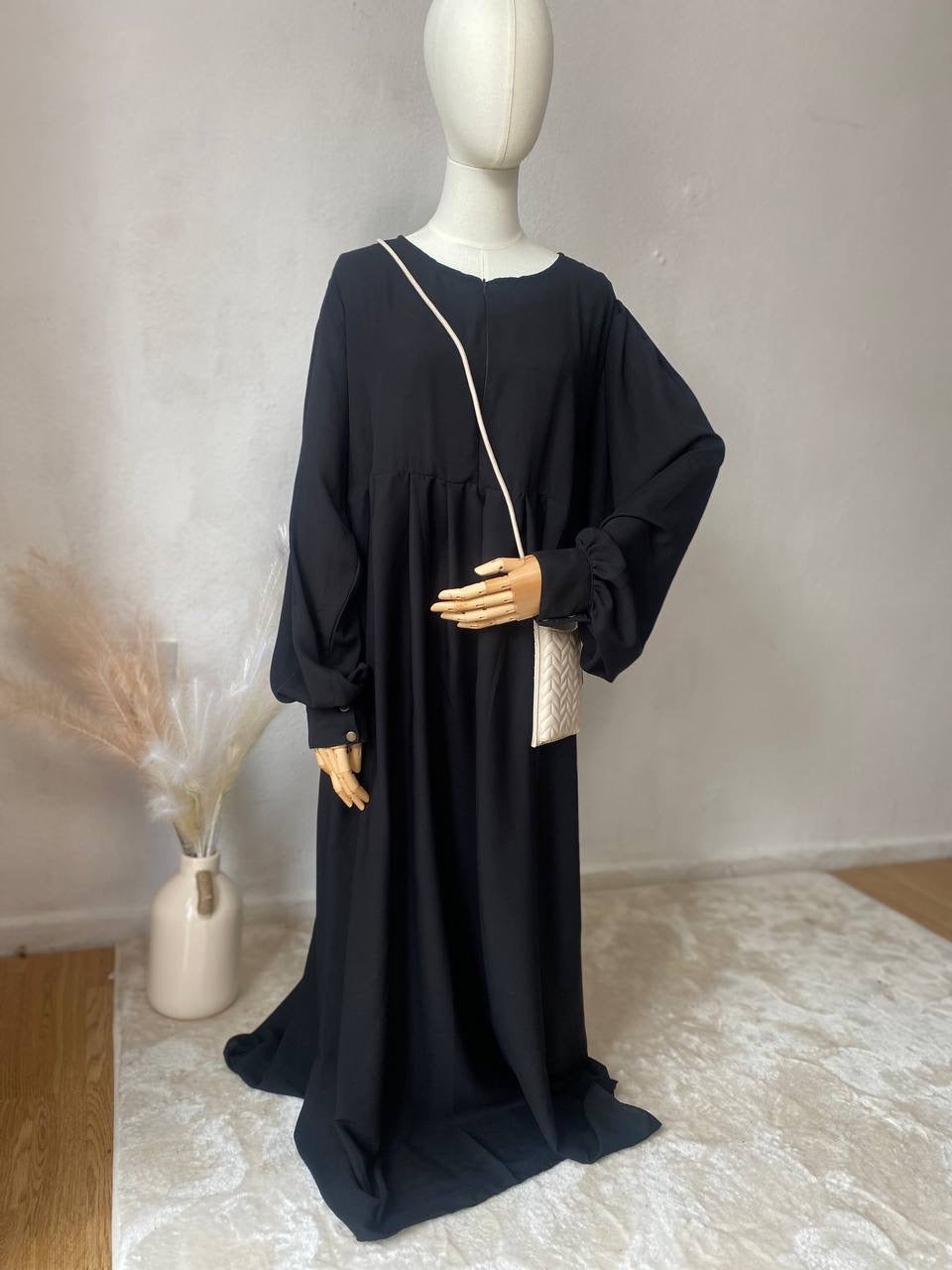 A mannequin displaying a black Russian abaya with long puffed sleeves, a high neckline, and a side pocket.