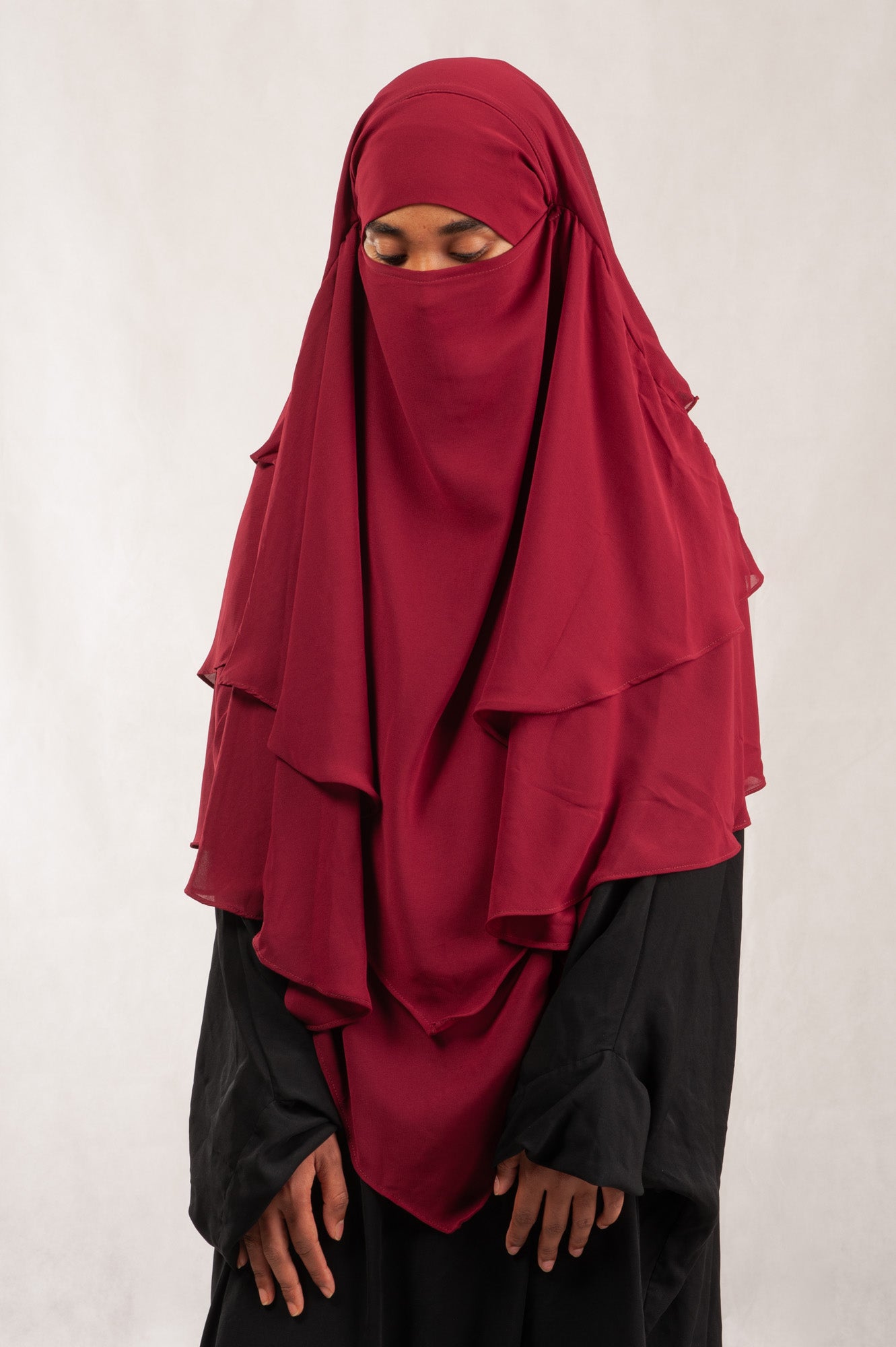 Person wearing a red hijab and black outfit on a white background