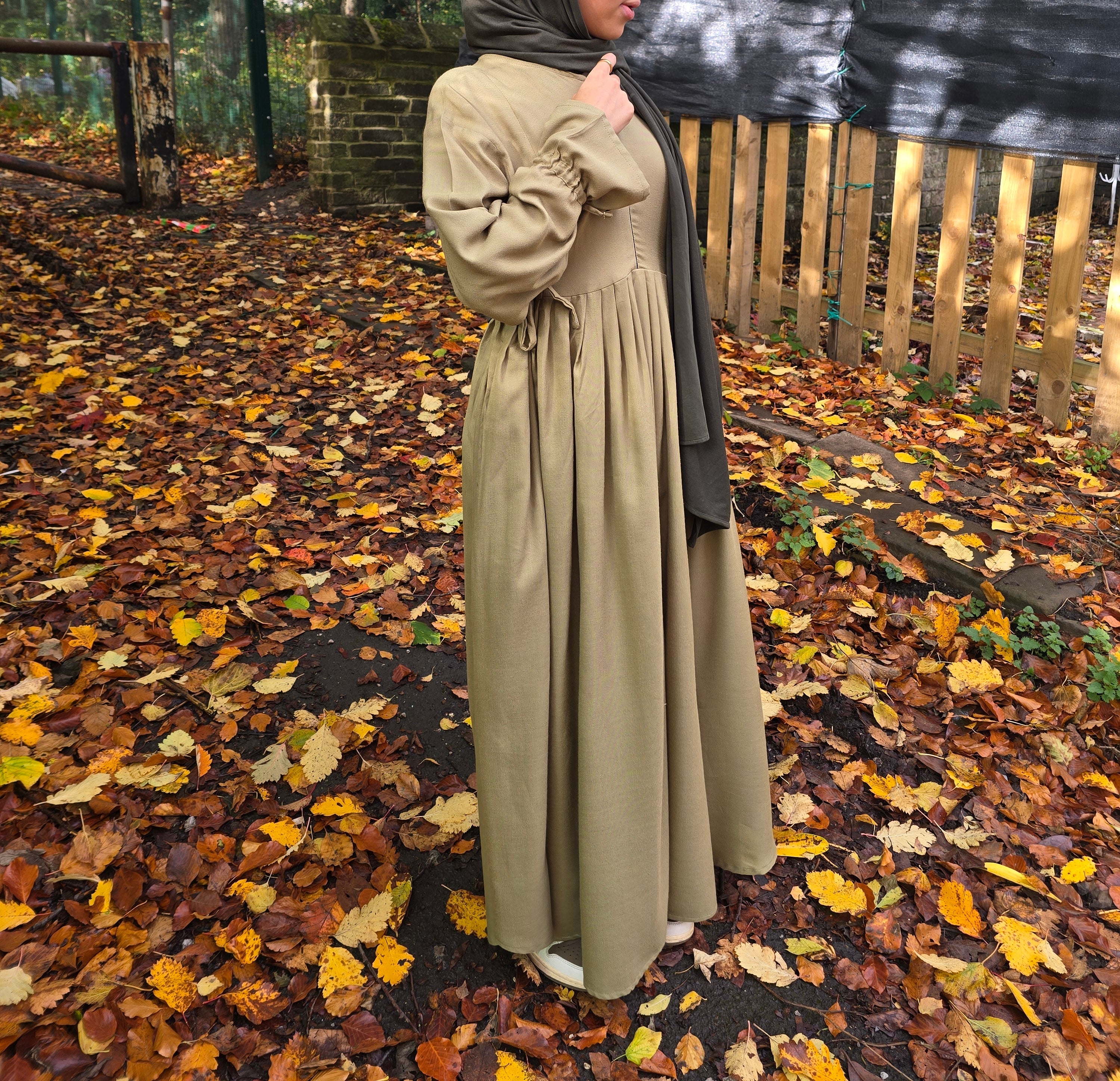 Person wearing a cotton abaya and headscarf standing on a path with autumn leaves