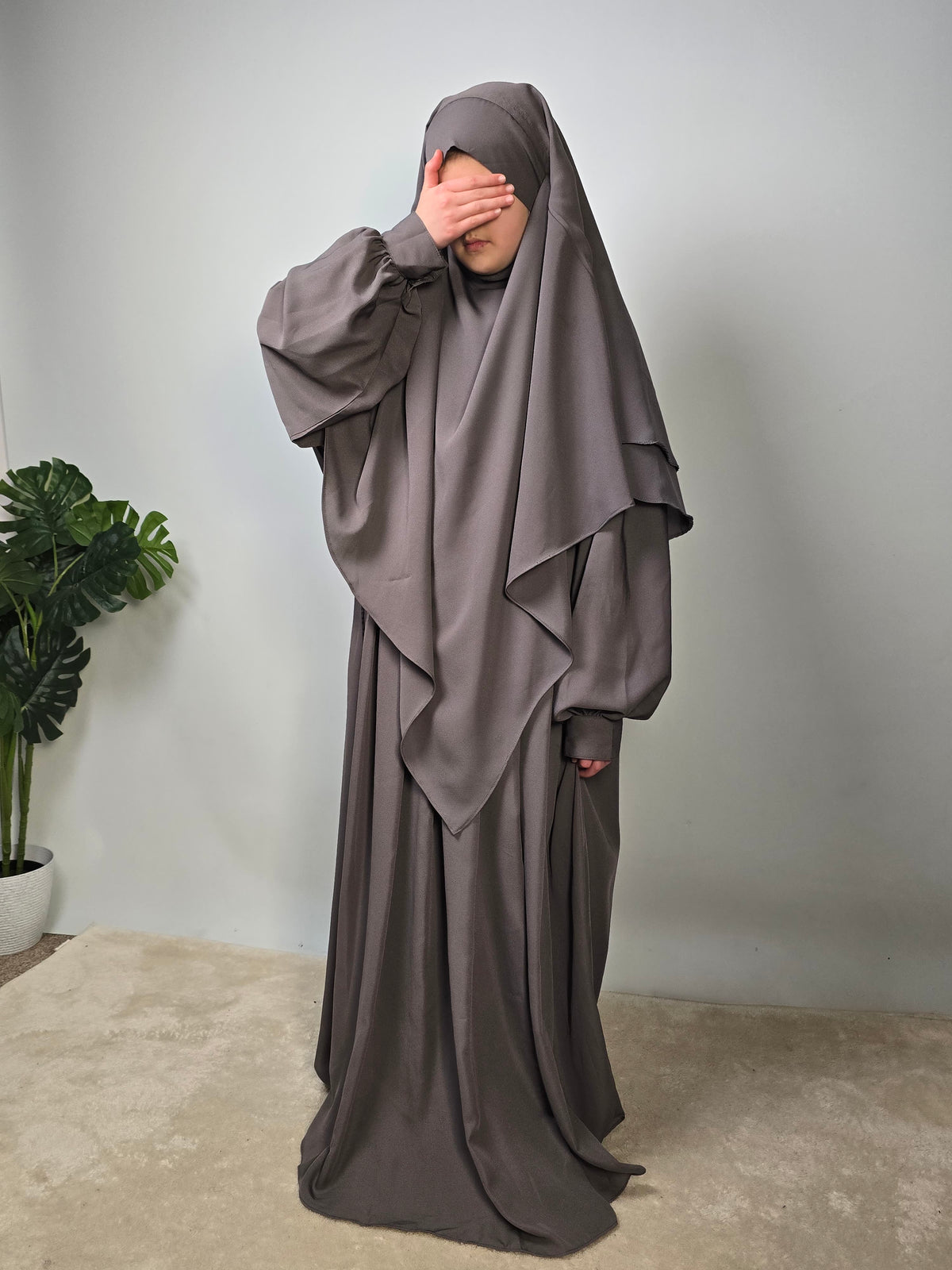 Person wearing a gray abaya and khimar set standing against a plain background