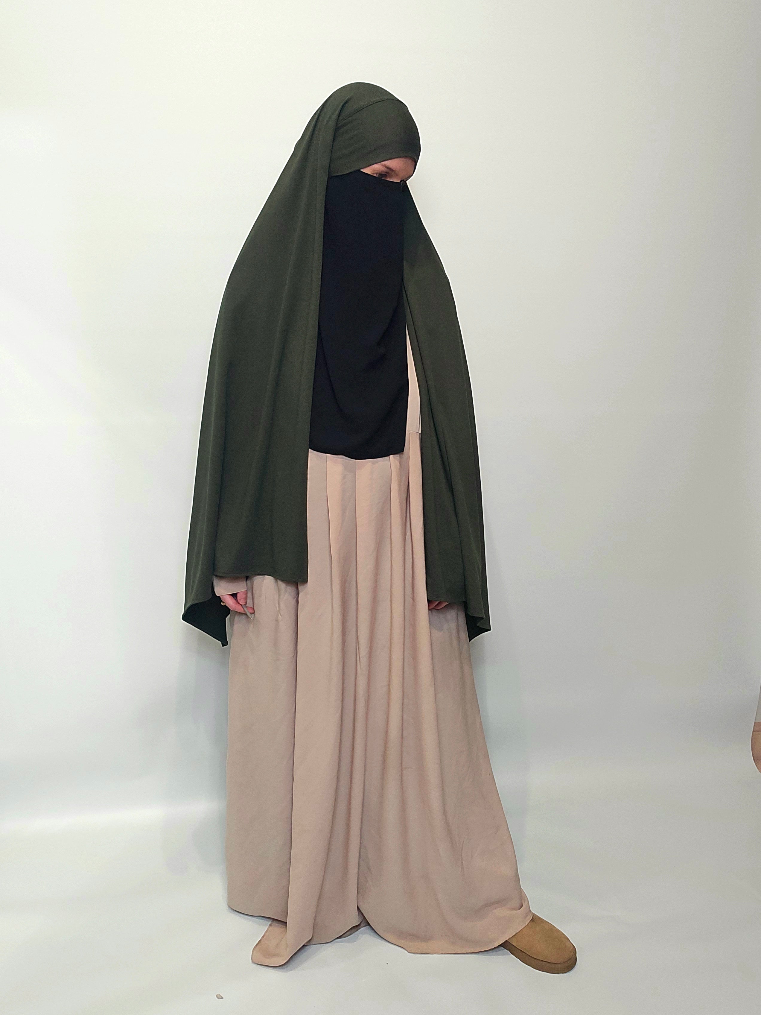 Person wearing a green hijab, black half niqab , beige abaya and brown winter boots on a white background