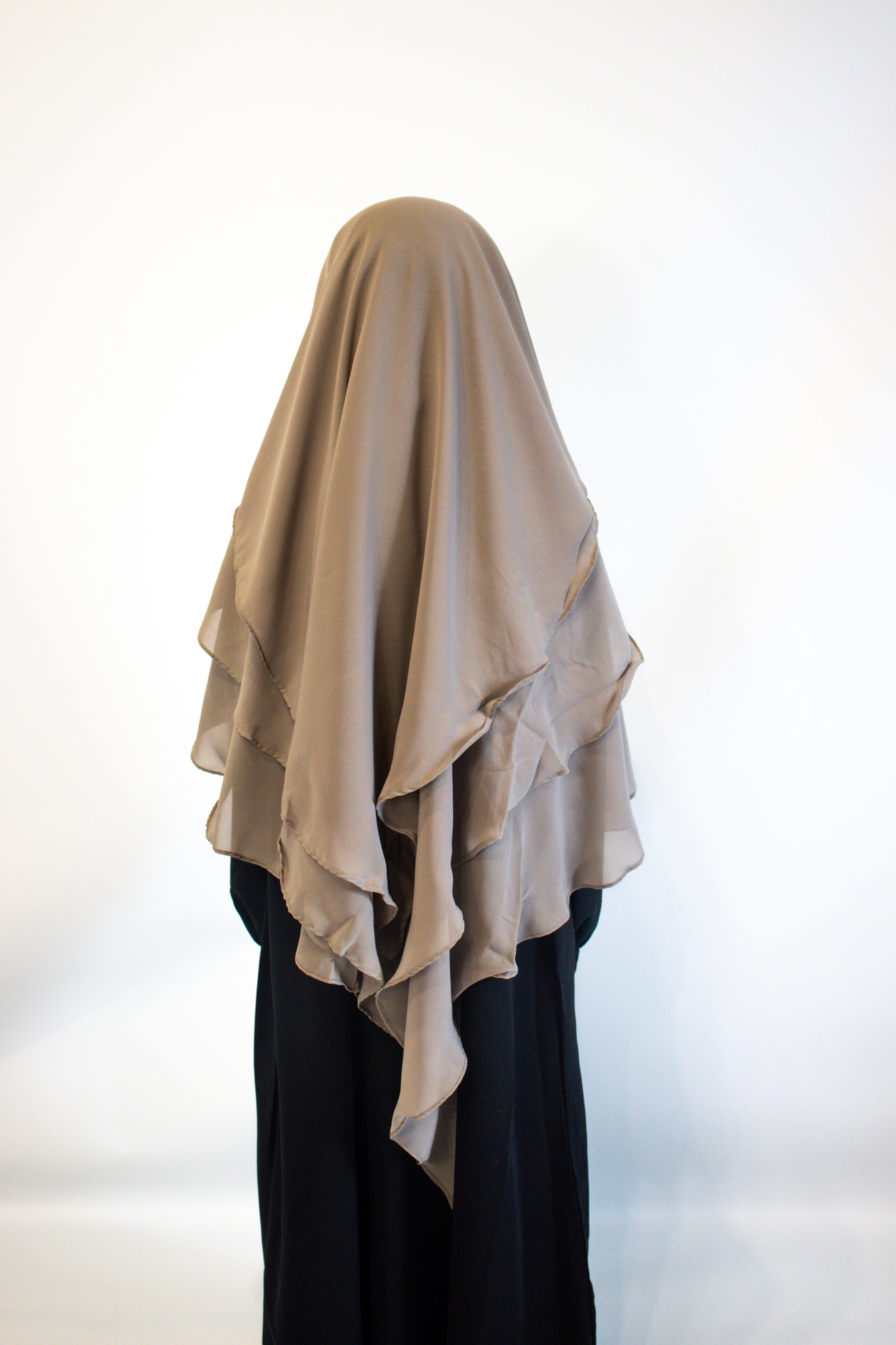girl wearing a taupe girl hijab and black abaya on a white background