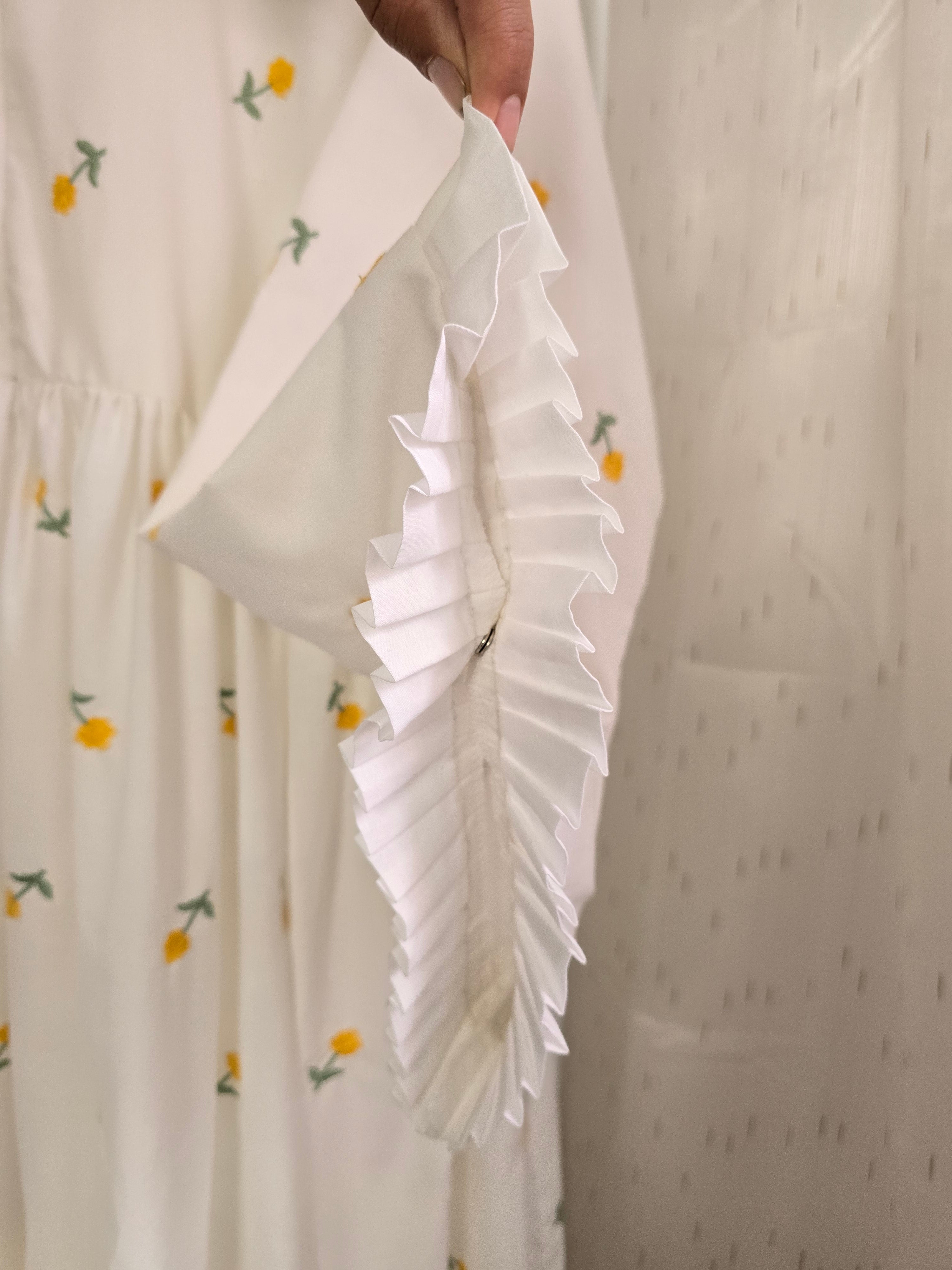 Close-up of a white fabric with floral patterns held by a hand against a neutral background.