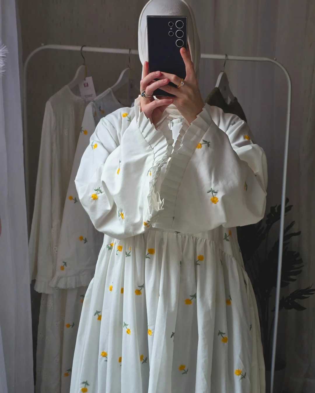 Person wearing a white dress with yellow floral patterns in a clothing store.