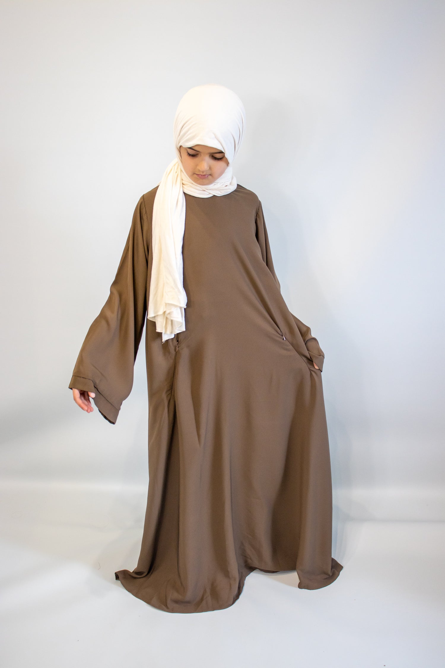 Girl wearing a brown abaya with a white hijab on a white background 