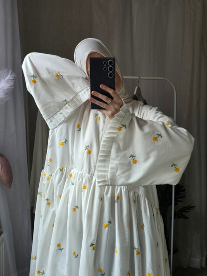 Person wearing a white dress with floral patterns, taking a mirror selfie.
