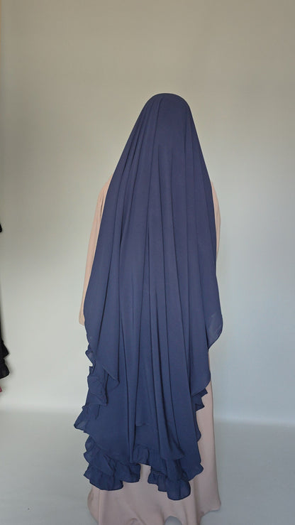 A navy blue chiffon hijab with layered ruffles, draped over a mannequin from the back against a plain light gray background.