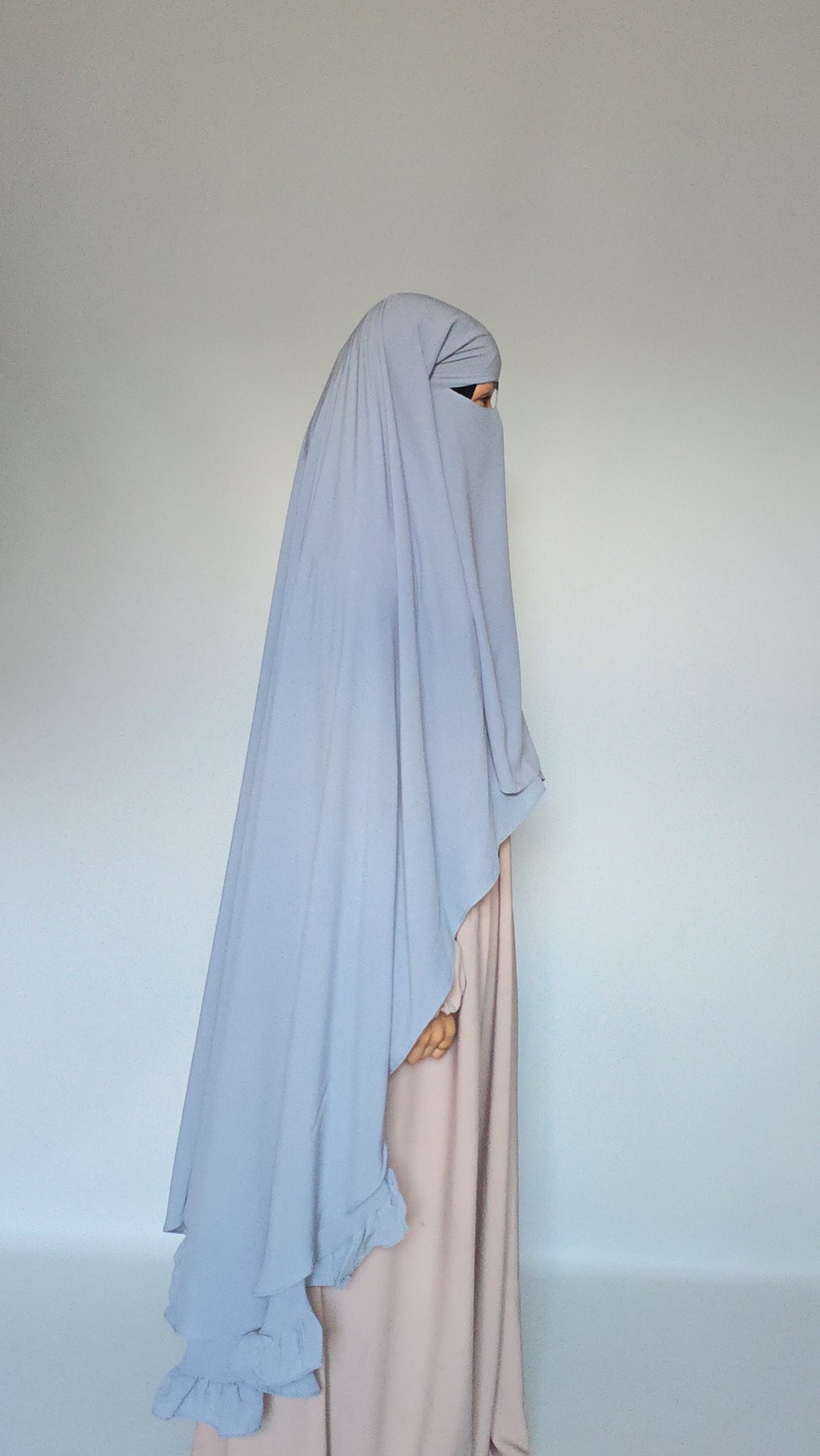 WOMEN WEAING A SKIES BLUE 3 LAYER GARMENT OVER HER HEAD COVERING HER BODY WITH A CREAM ABAYA AND ON A WHITE BACKGROUND 
