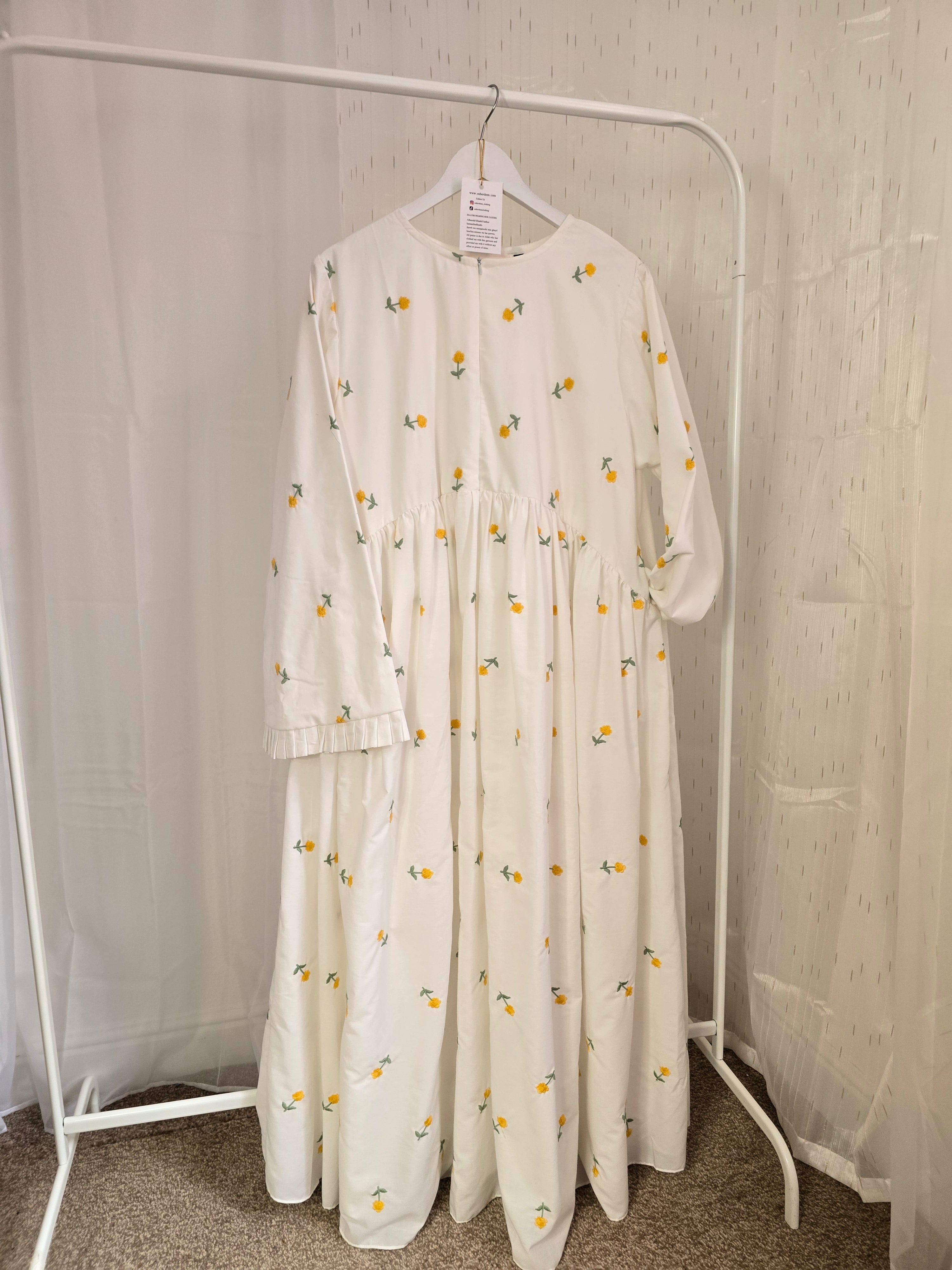 White dress with floral pattern on a white rack against a neutral wall.