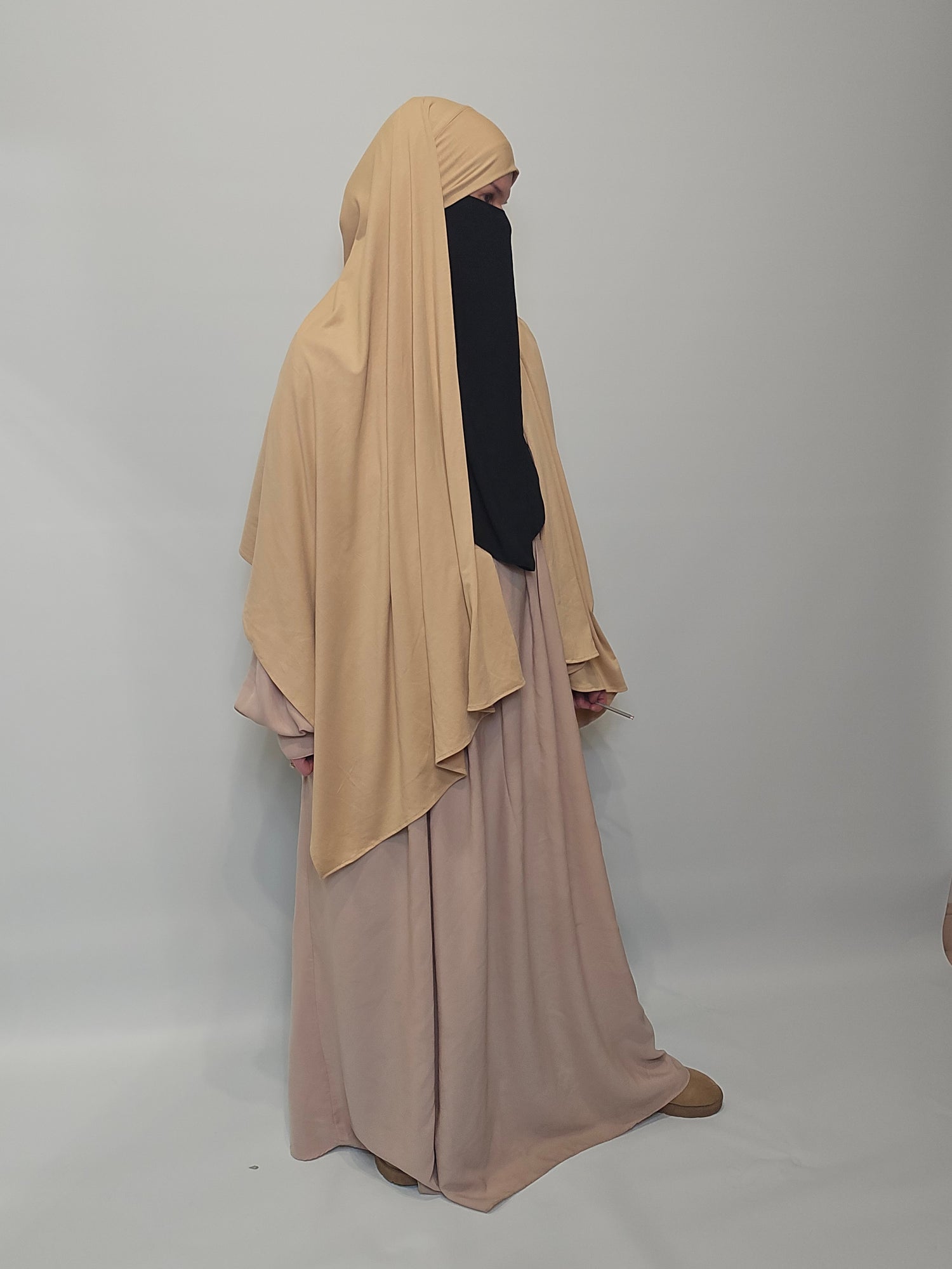 Women in beige maxi jersey hijab and a beige abaya on a white background 