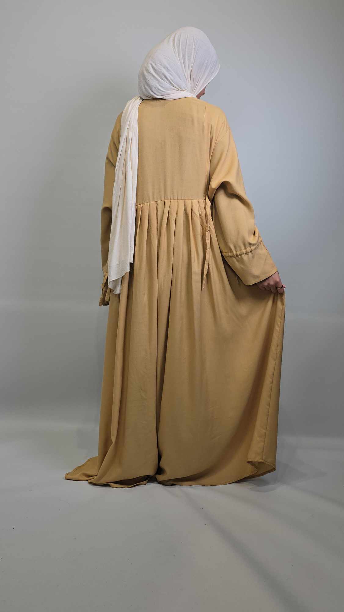 Person wearing a  long abaya with a white headscarf on a gray background