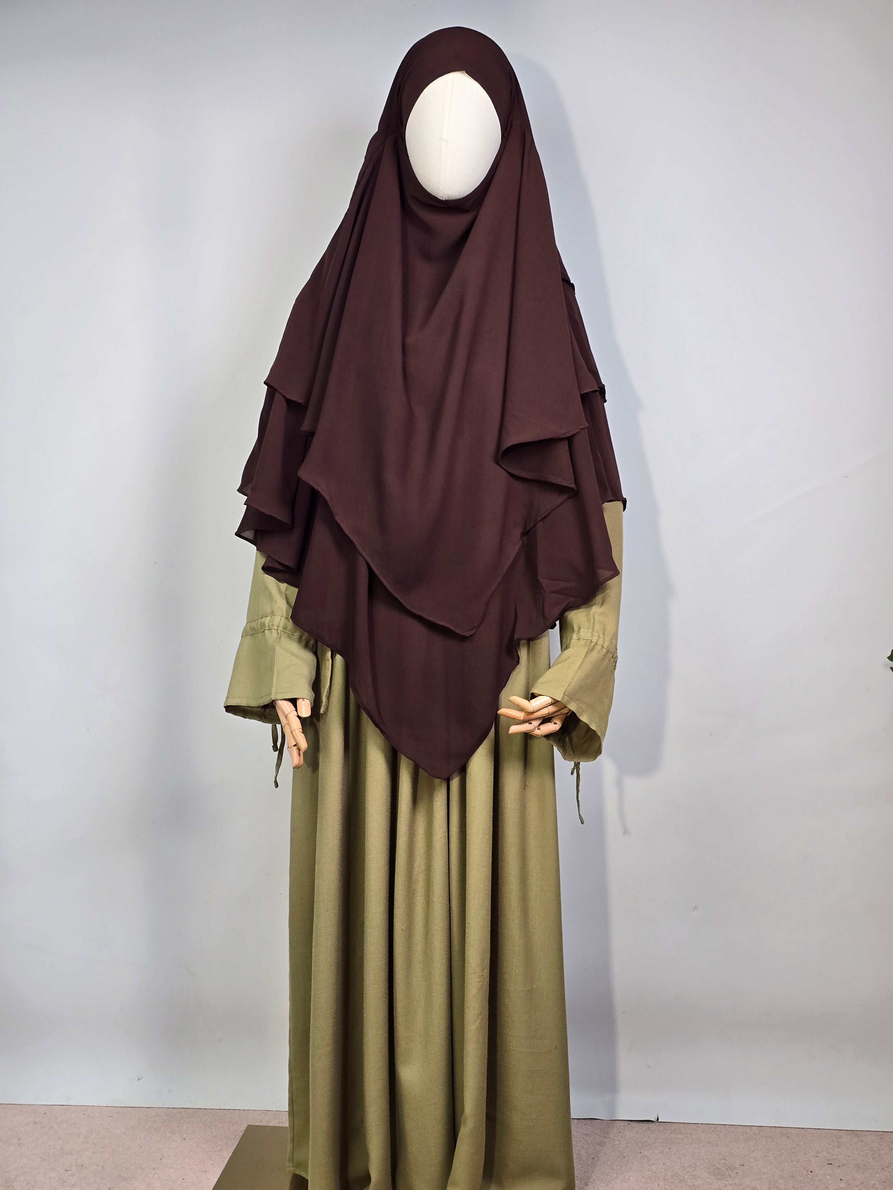mannequin wearing a dark brown layered chiffon hijab khimar with a green dress on a white background 