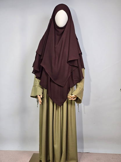 mannequin wearing a dark brown layered chiffon hijab khimar with a green dress on a white background 