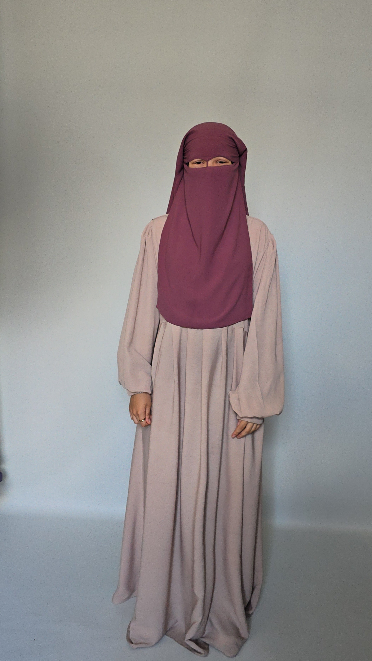 Woman wearing a dusky pink niqab and cream abaya on a wite studio background 
