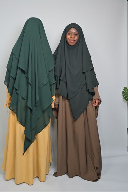 Two women wears different shades of green chiffon khimars with abayas on a white background 