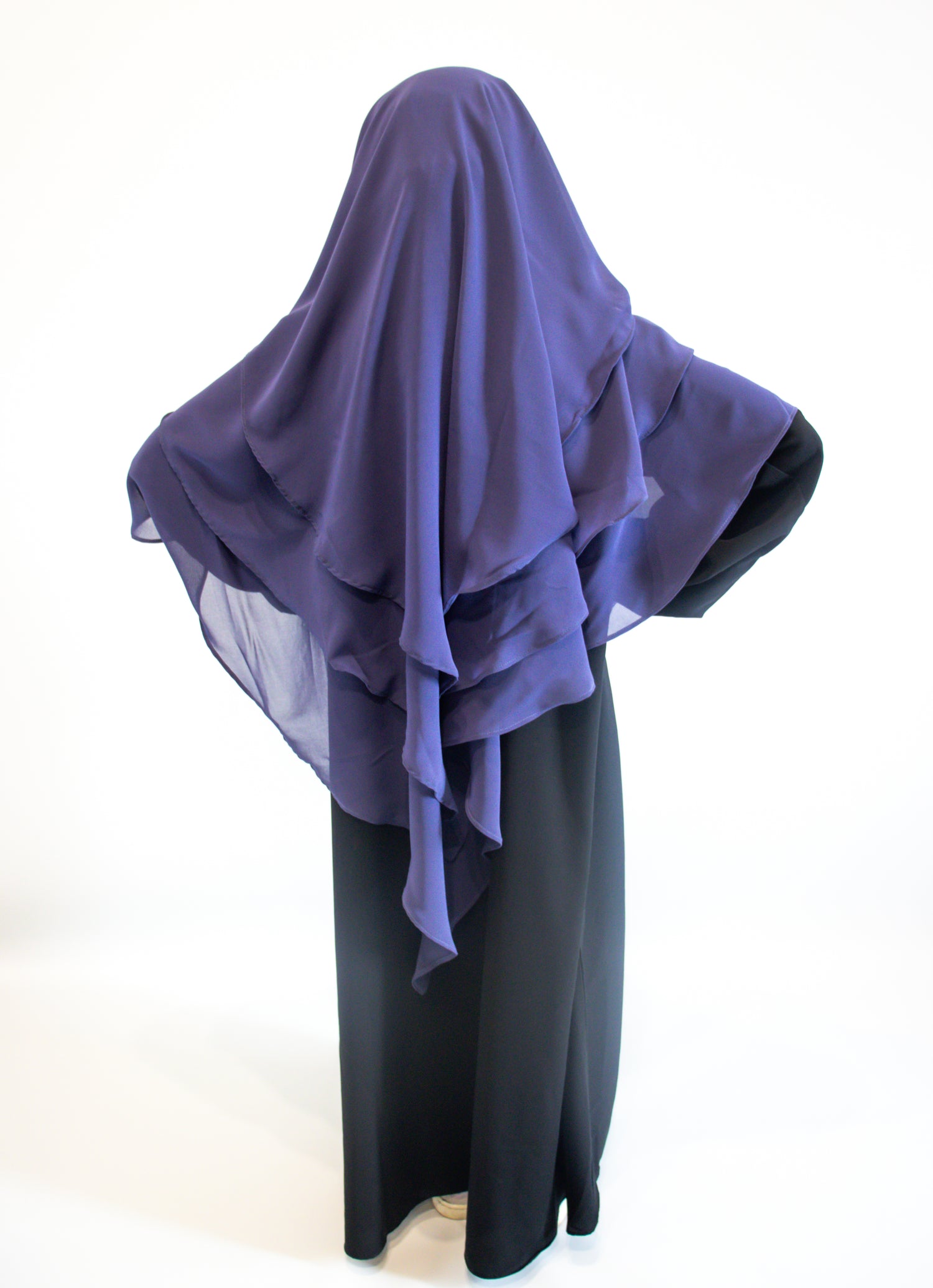 A girl wearing indigo purple hijab over a black outfit on a white background