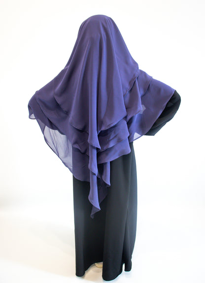 A girl wearing indigo purple hijab over a black outfit on a white background