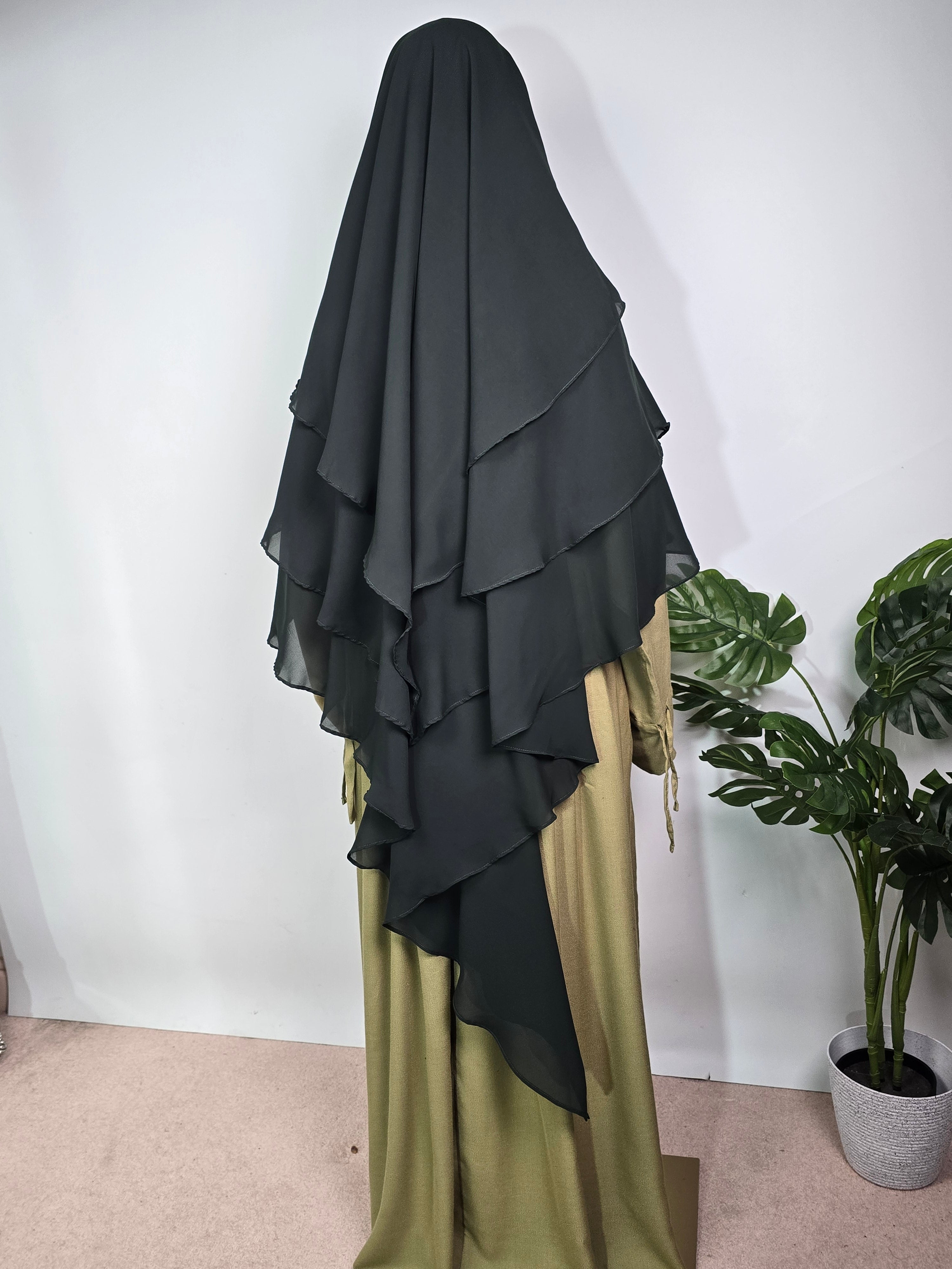 women in forest green 3 layer khimar pair with a sage green abaya on a white background with a plant