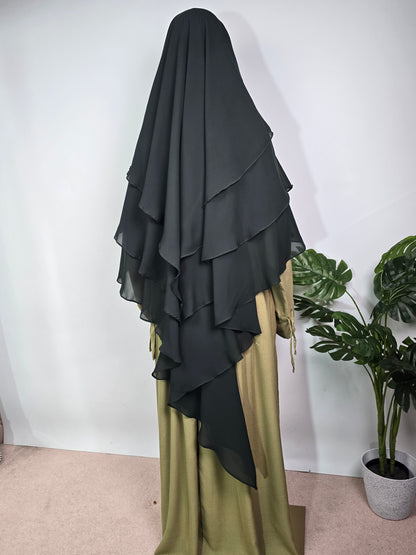 women in forest green 3 layer khimar pair with a sage green abaya on a white background with a plant