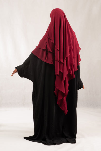Person wearing a black abaya with a red hijab on a white background