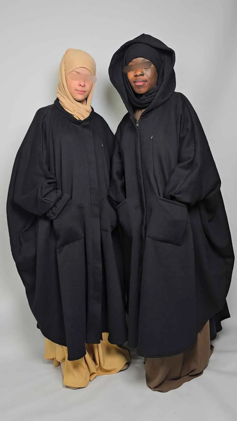 Two women in black oversized poncho Abaya fleece stood on a white background 