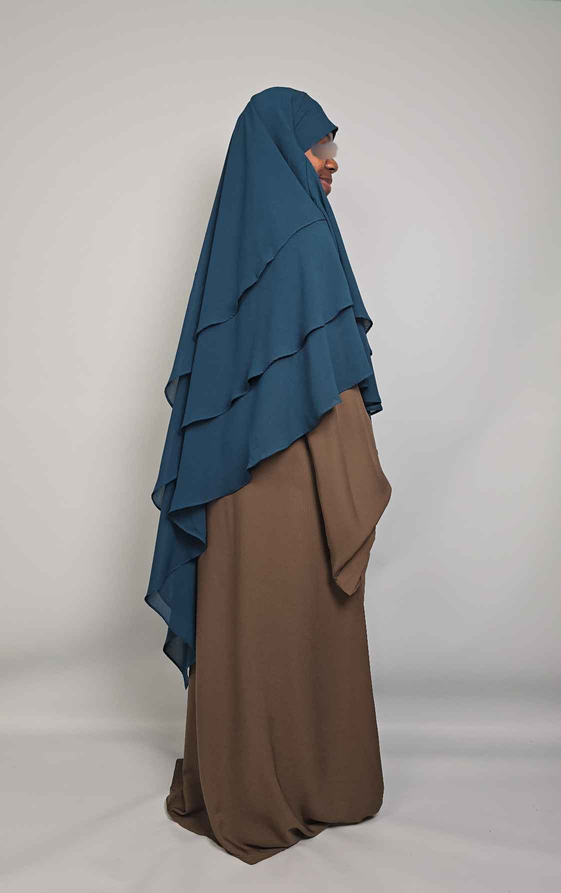 Person wearing a layered hijab with blue and brown colors on a plain background