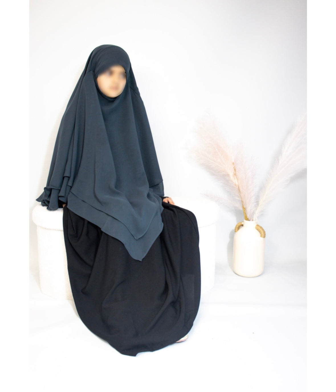 Person wearing a teal blue hijab and black outfit on a white background