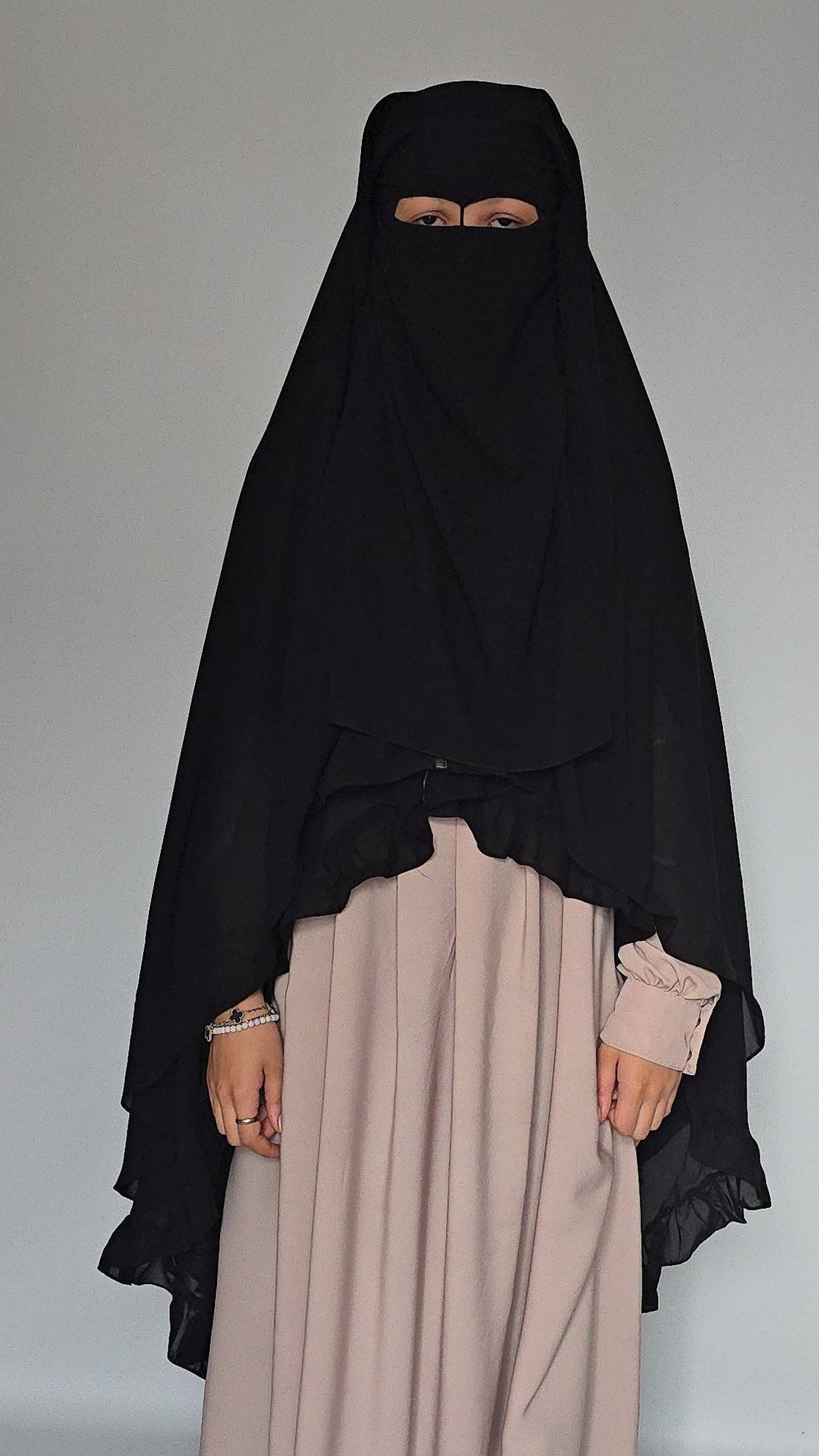 Women wearing long black niqab cover full face and body with a cream dress on a white background 