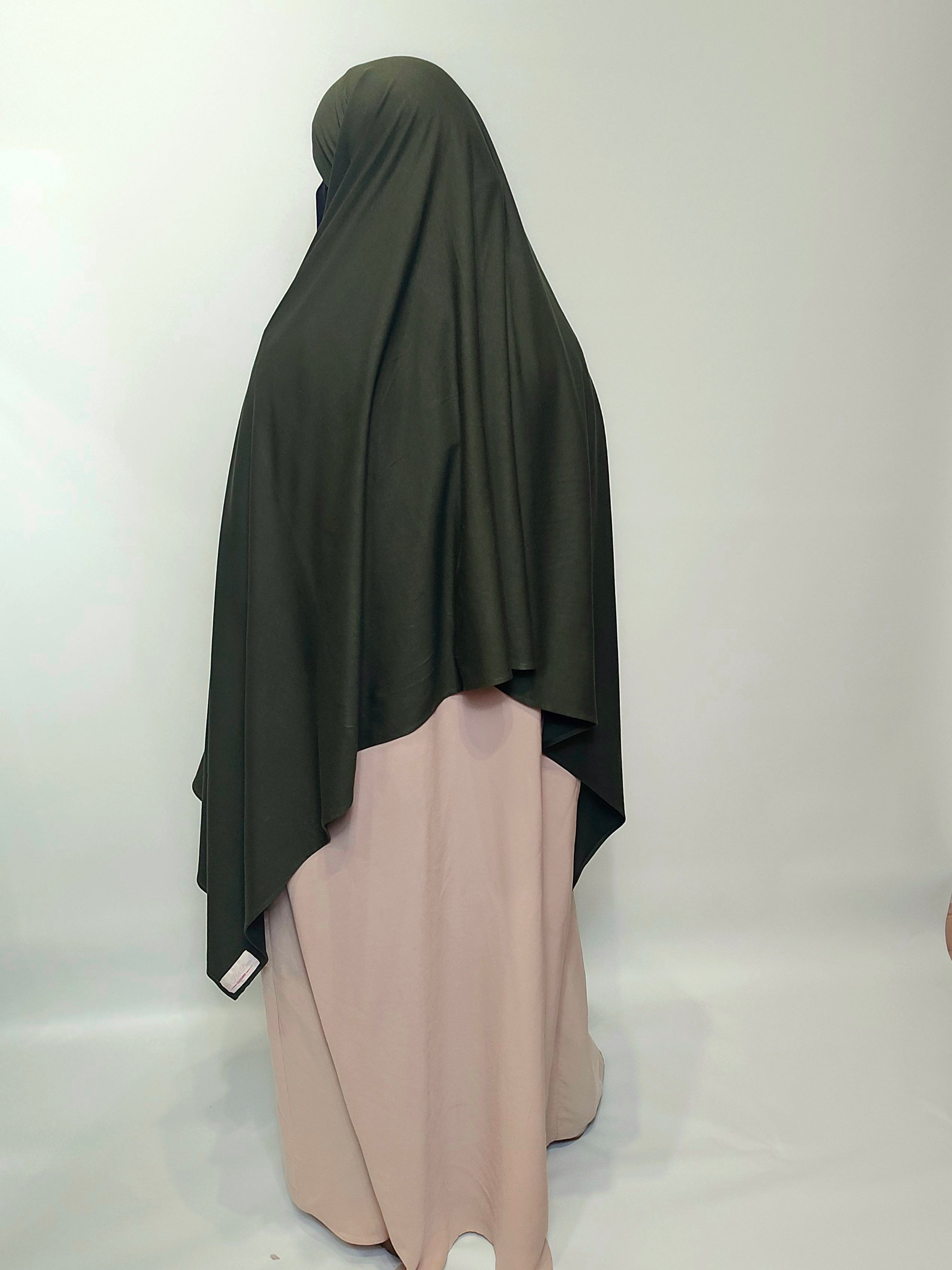 Person wearing a dark green hijab and beige dress on a white background