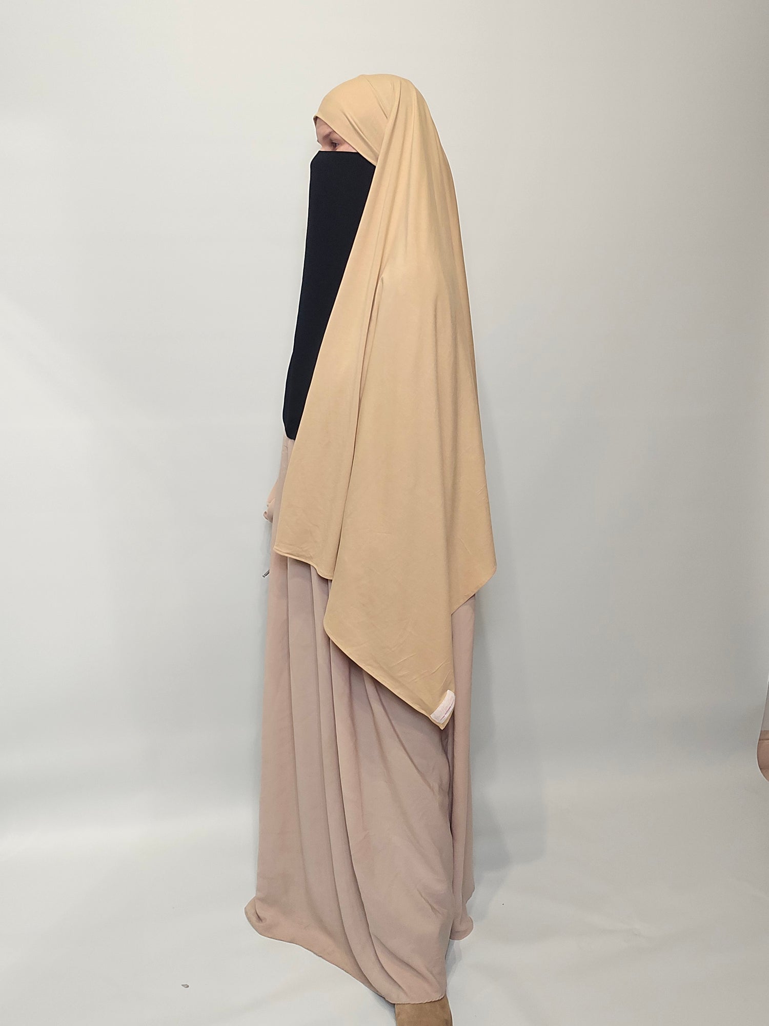 Person wearing a beige dress with a black niqab and a beige hijab  on a white background