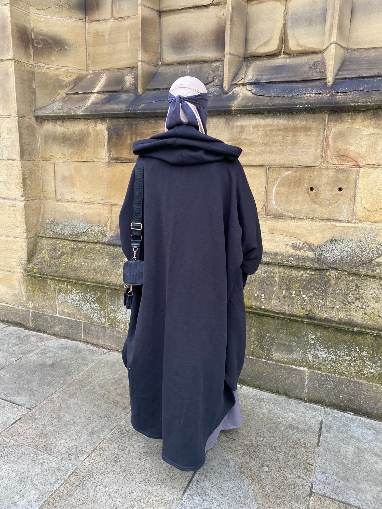 woman against a stone wall in a oversized abaya coat hoodie 
