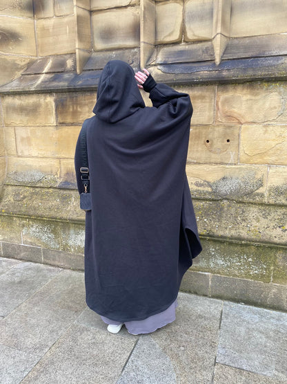 women in full length black modest abaya coat against a stone wall 