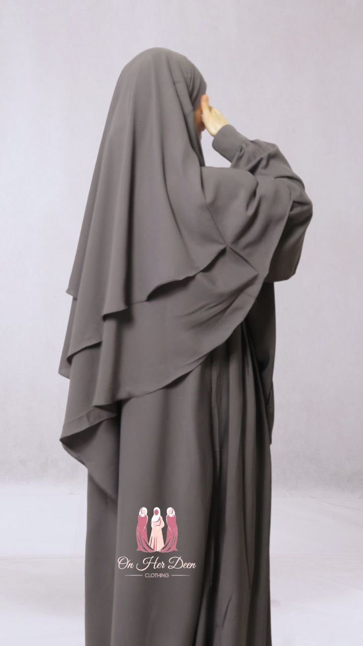 A woman wearing a gray two-layered diamond khimar with niqab ties, designed for full coverage of the face and body.