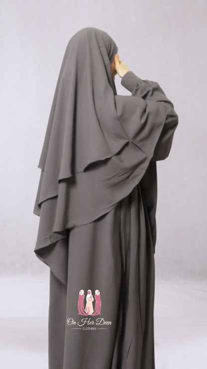 A woman wearing a gray two-layered diamond khimar with niqab ties, designed for full coverage of the face and body.