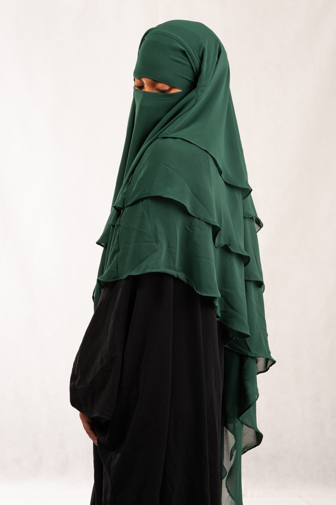 Person wearing a green layered hijab and black dress against a white background