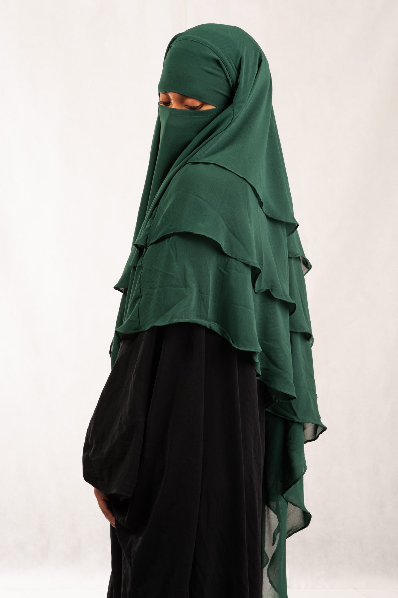 Person wearing a green layered hijab and black dress against a white background