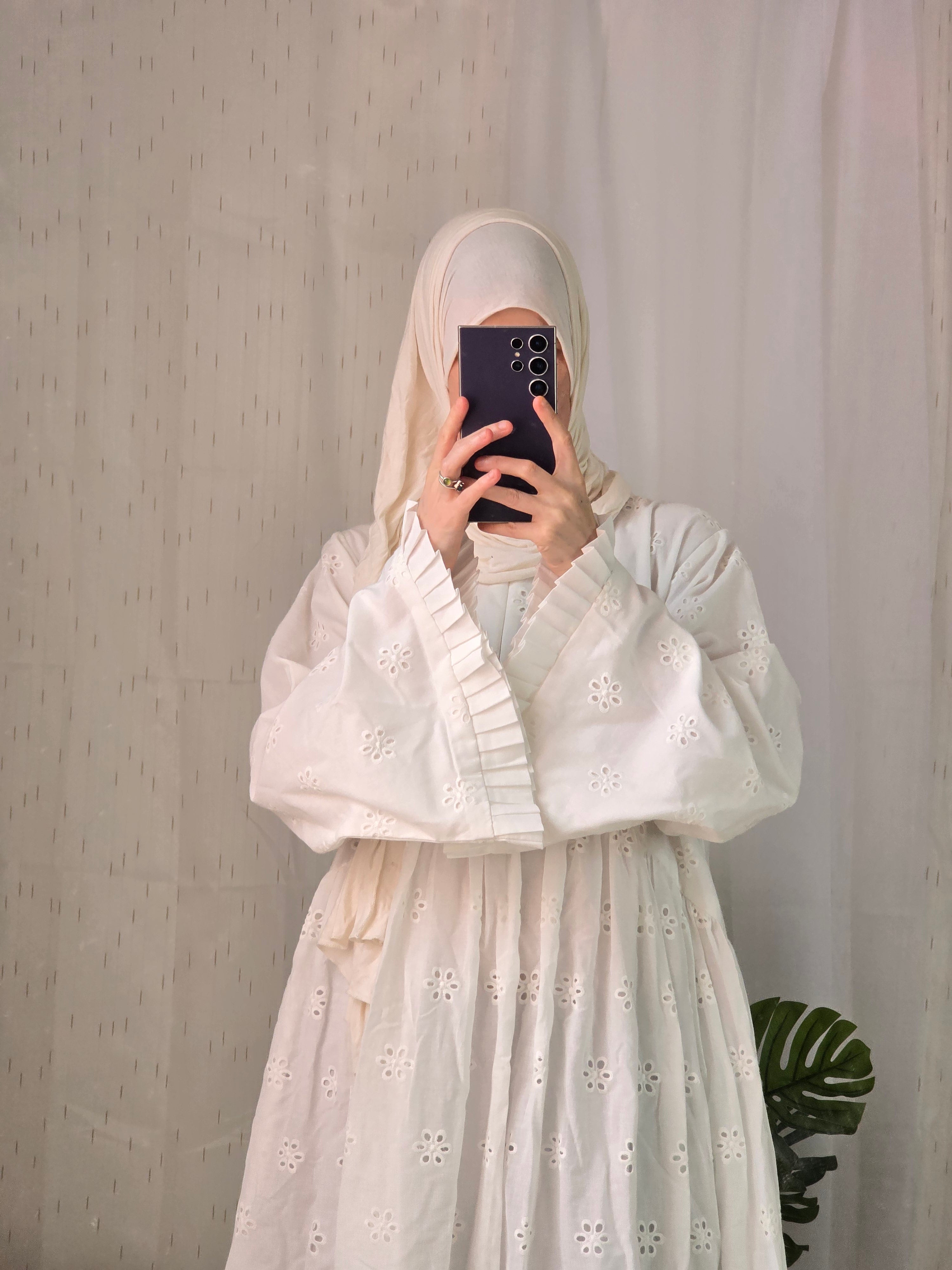 Person wearing a light-colored abaya dress with floral patterns on a plain background