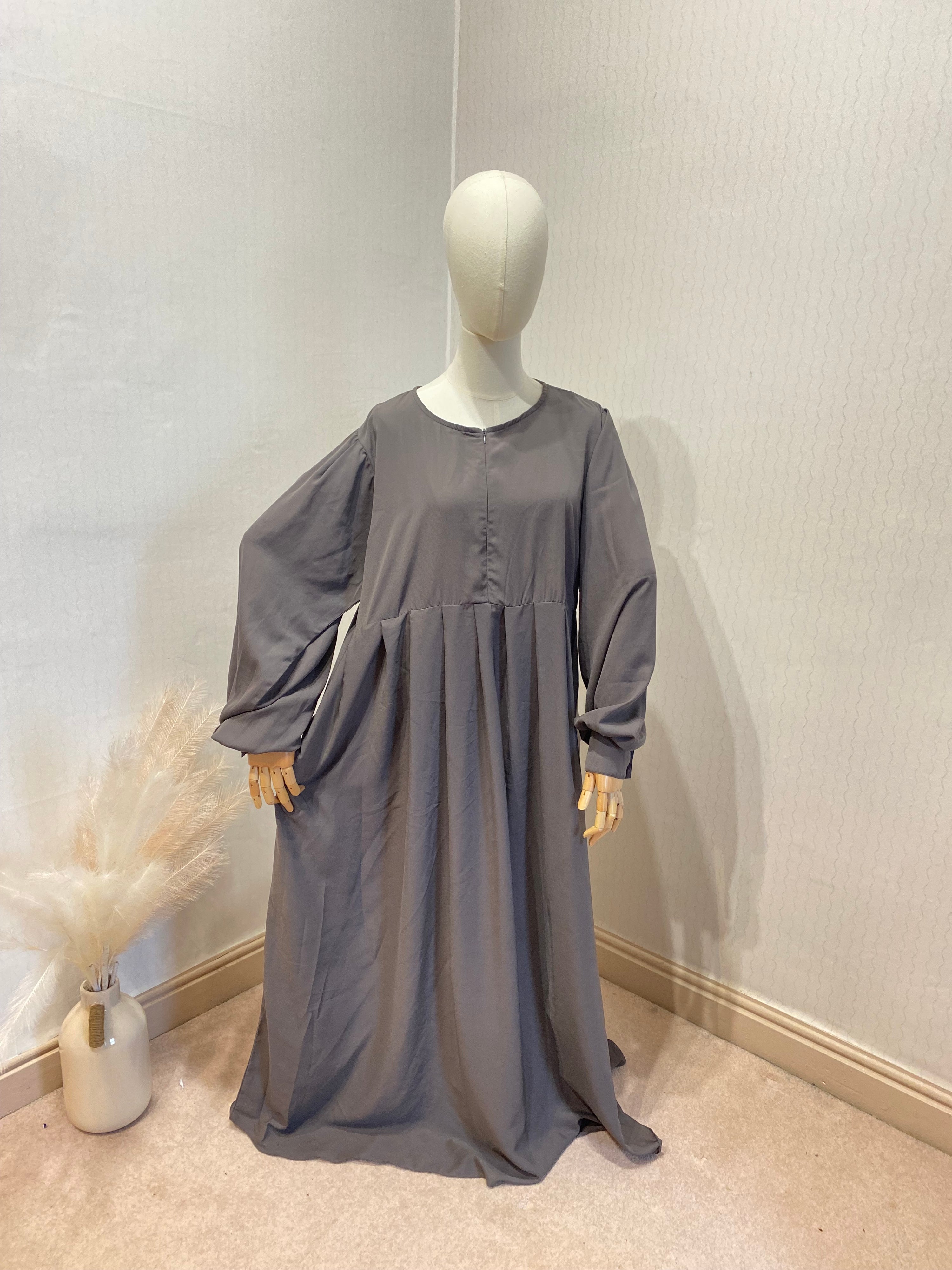 mannequin stood wearing a grey abaya with pockets 

