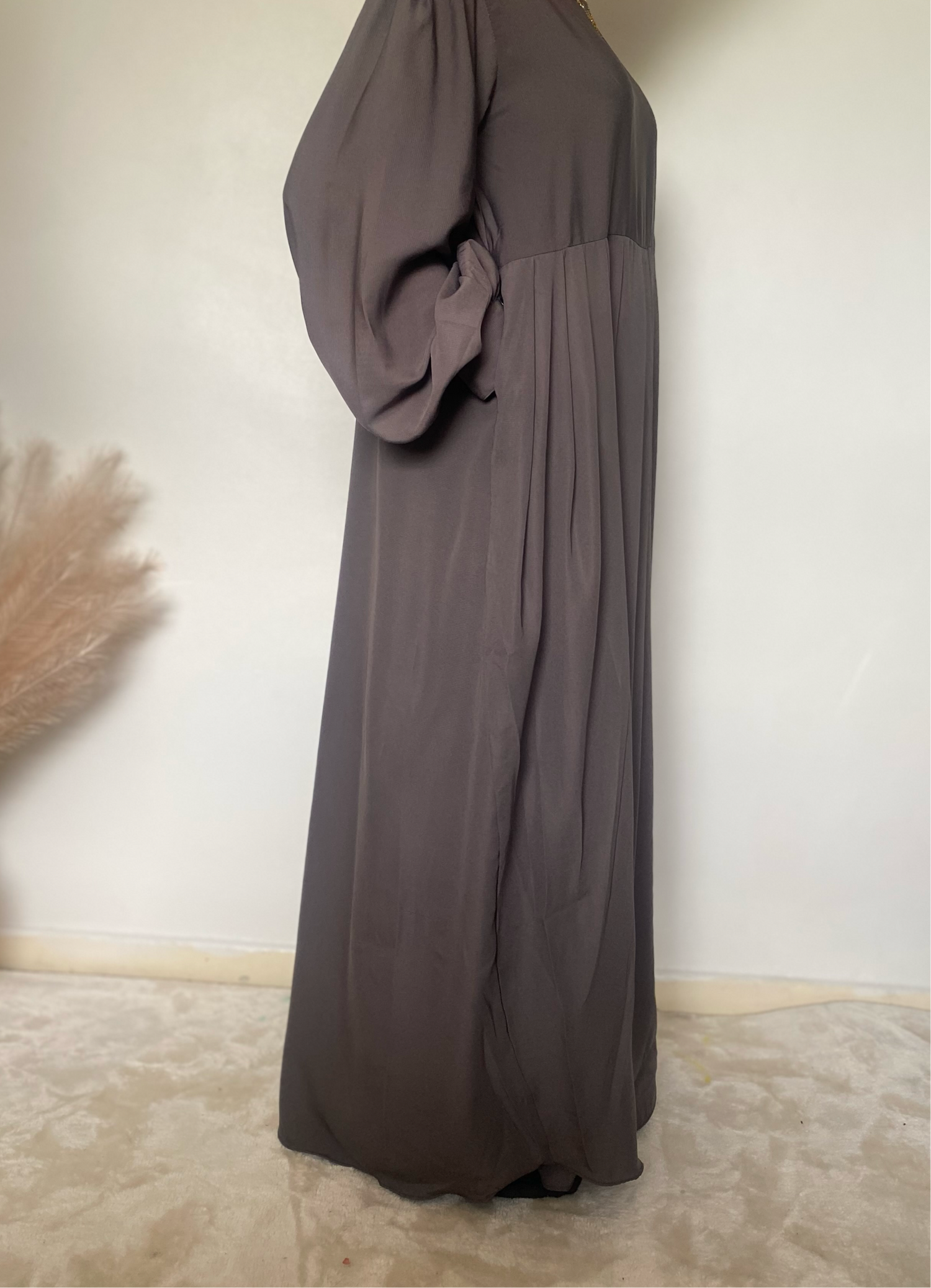 teenager stood in a grey abaya with pockets and puffy sleeves on a white background 
