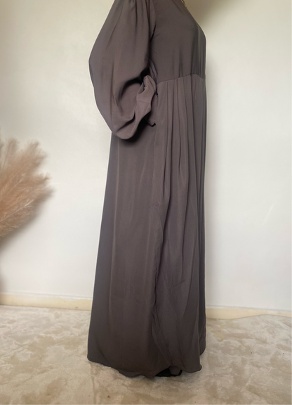 teenager stood in a grey abaya with pockets and puffy sleeves on a white background 