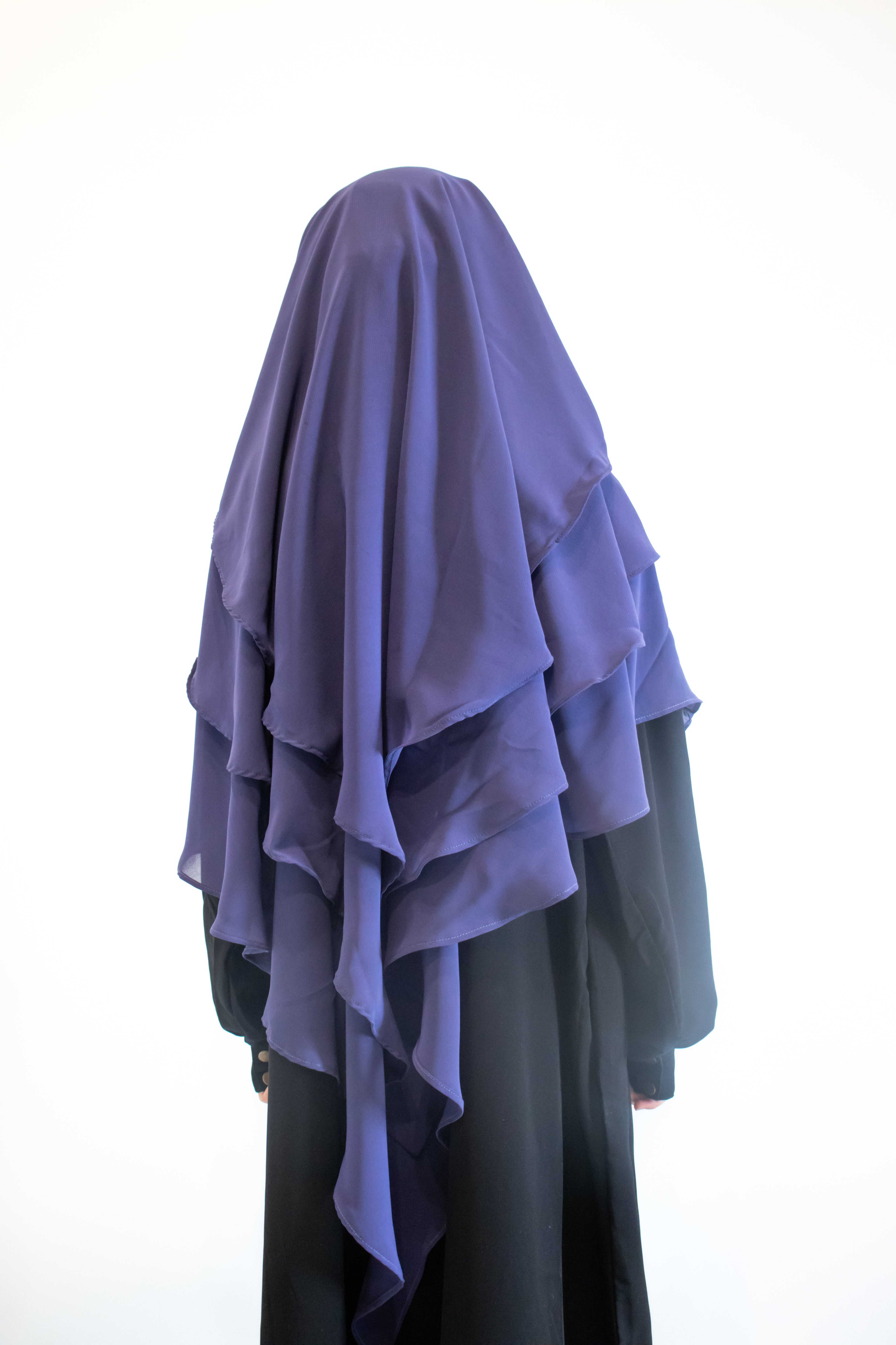 Girl wearing a indigo Purple hijab draped over a black abaya on a white background