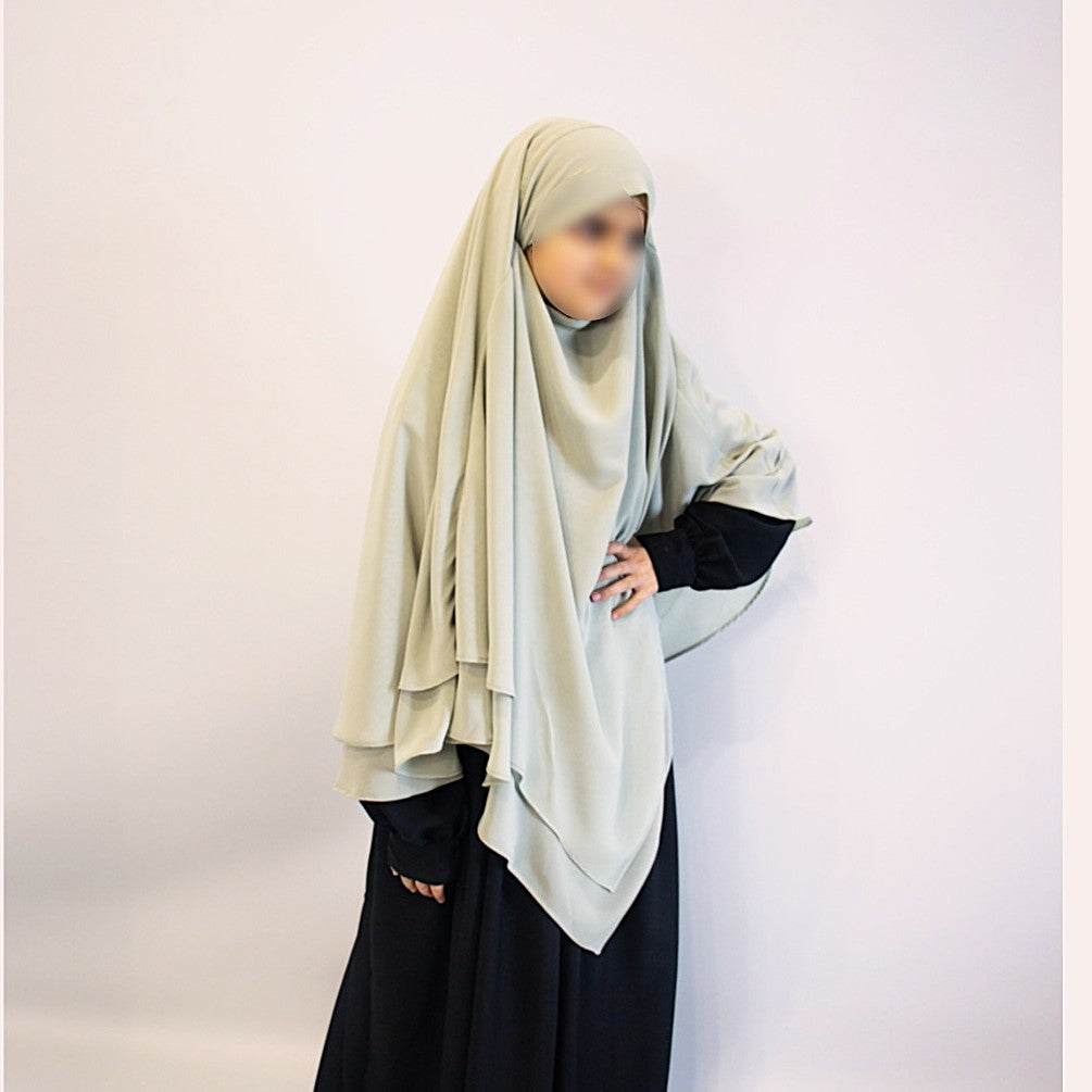 Person wearing a light-colored hijab and black clothing on a plain background