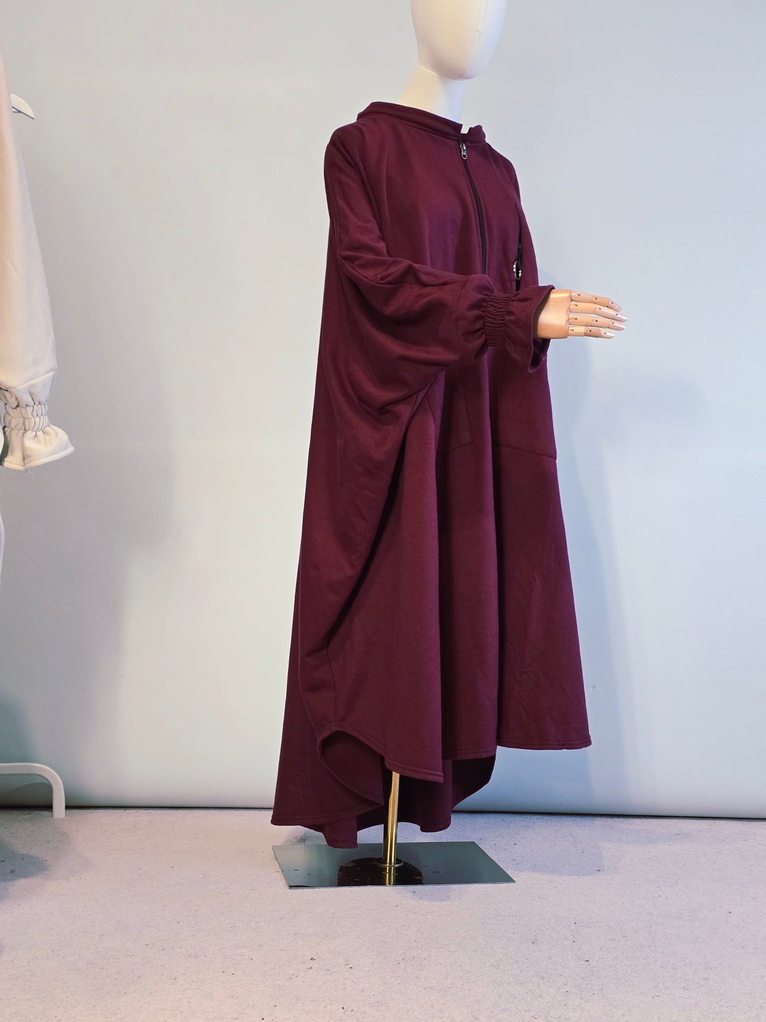 Maroon coat on a mannequin against a light gray wall