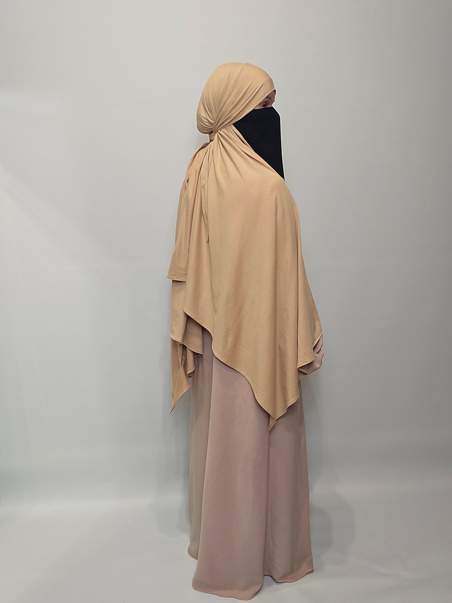 Beige abaya with matching hijab on a plain background