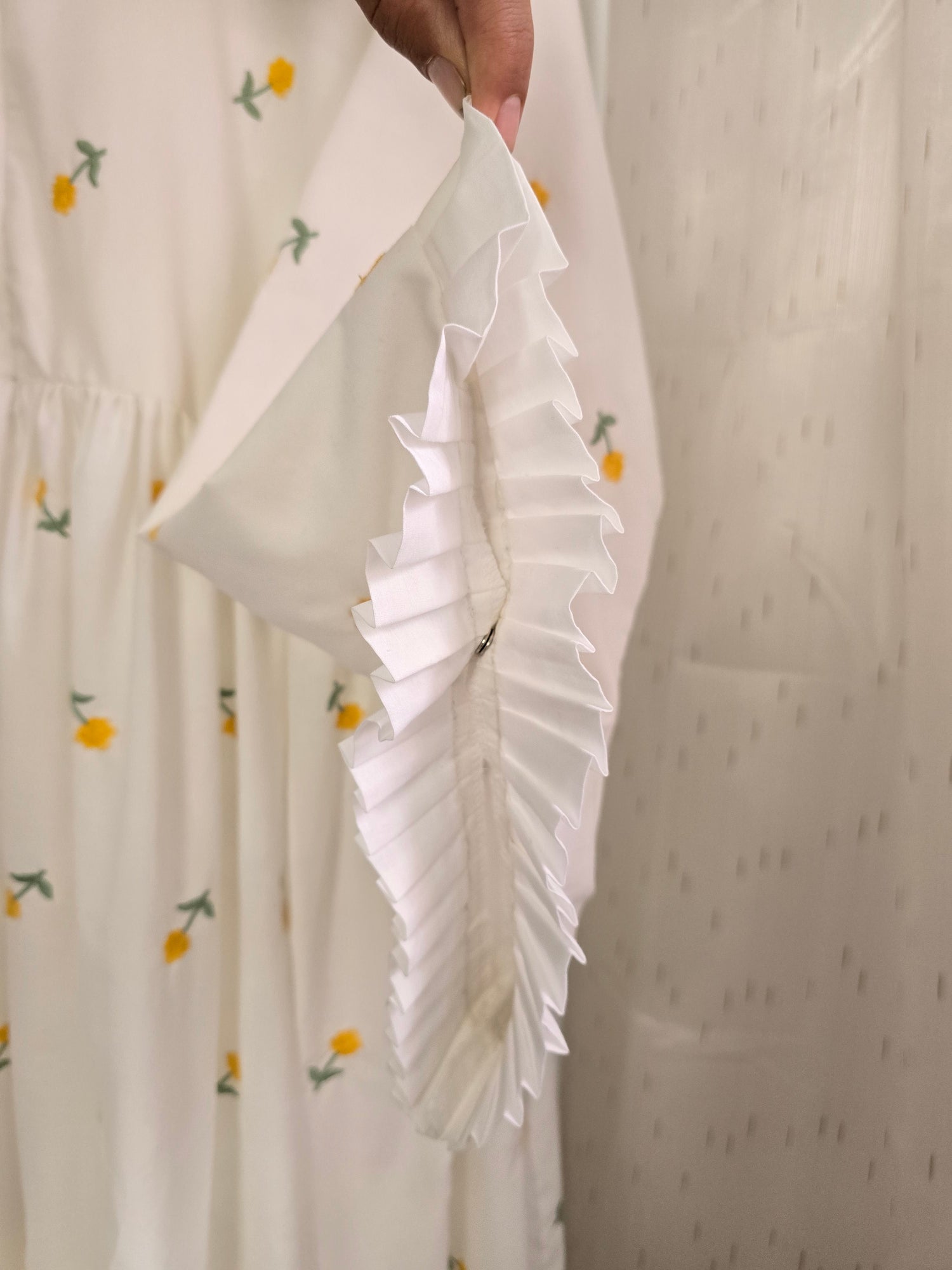Close-up of a white fabric with floral patterns held by a hand against a neutral background.