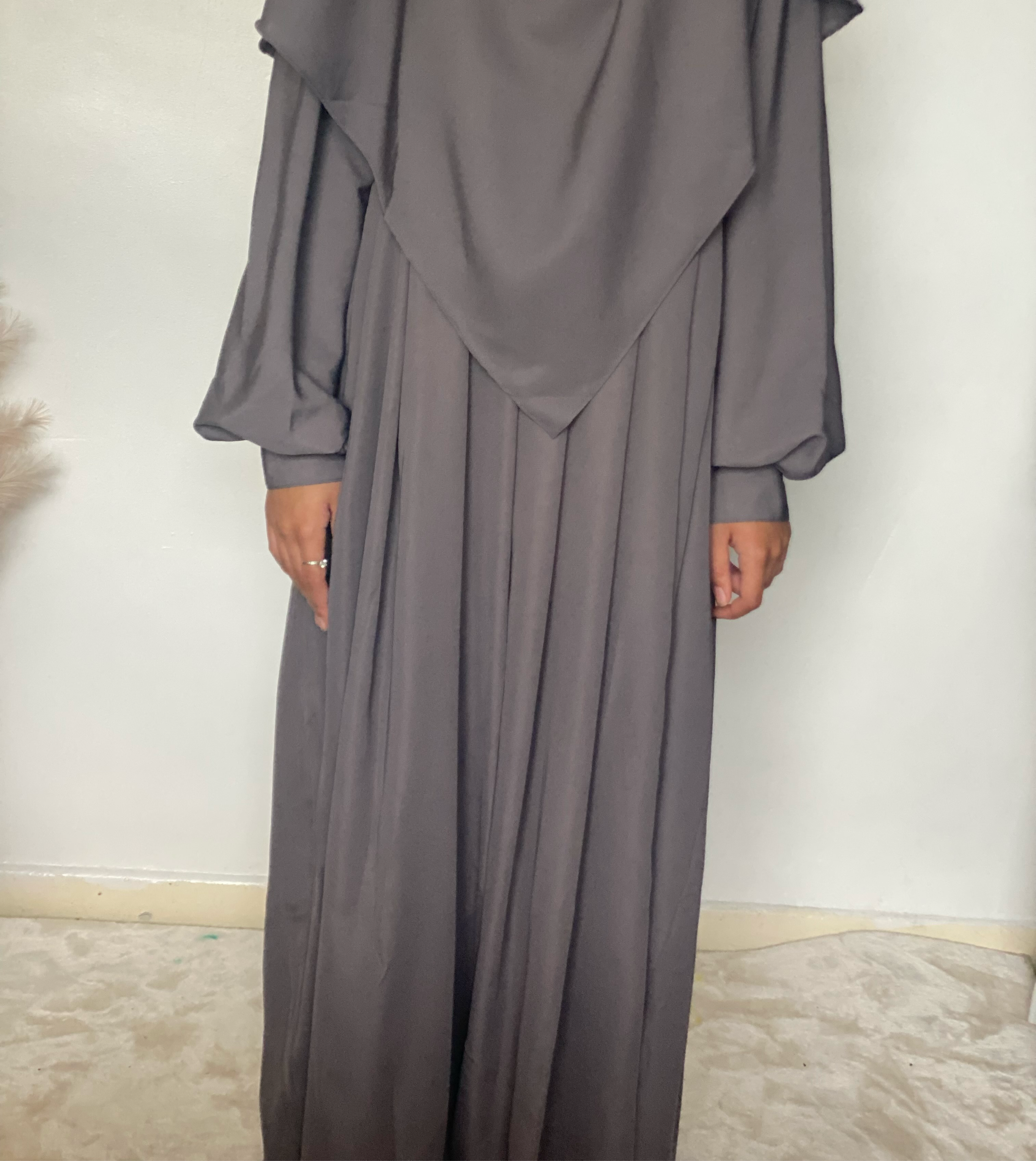 a girl in a two piece khimar abaya set in color grey indoors on a white background 
