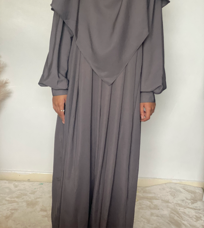 a girl in a two piece khimar abaya set in color grey indoors on a white background 
