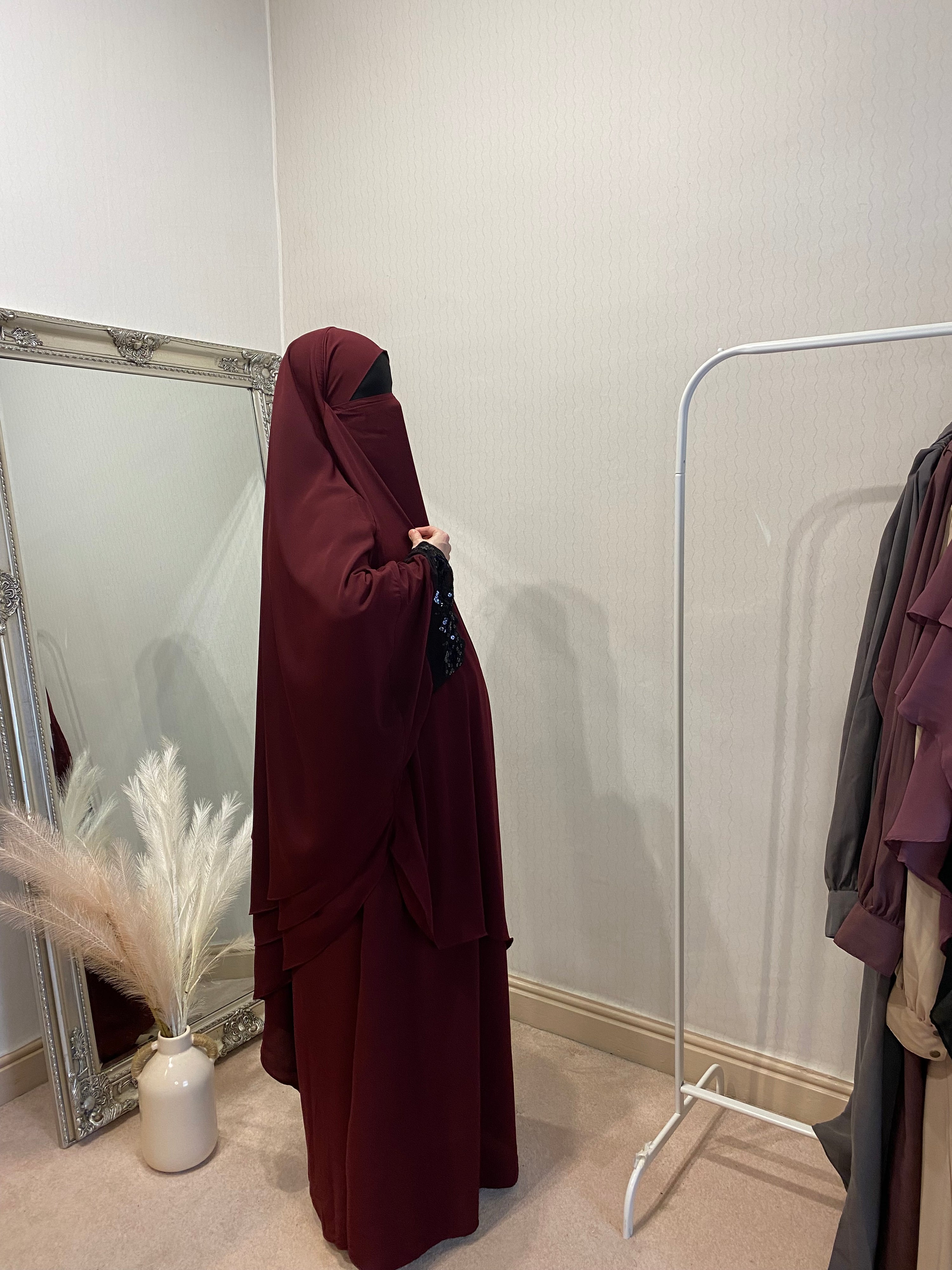 woman in a 3 layer two piece jilbab in a solid red color with a long mirror behind her 
